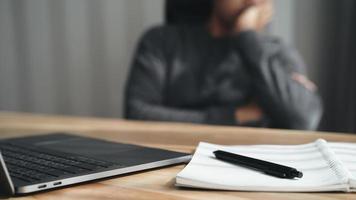 uomo d'affari stanco che lavora al computer portatile con blocco note e penna, appoggiando la testa a portata di mano, facendo gli straordinari, stressato e annoiato foto