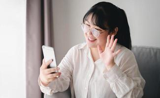 giovane donna asiatica che utilizza lo smartphone per la videoconferenza online con gli amici che agitano la mano facendo un gesto di saluto foto