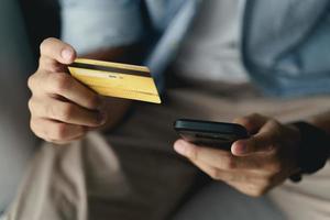 uomo in possesso di carta di credito e utilizzando smartphone per lo shopping online, internet banking, e-commerce, spendere soldi, lavorare da casa concetto foto