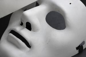 maschera facciale di carnevale bianca sdraiata, primo piano, foto orizzontale su sfondo scuro. maschera di plastica teatrale, oggetti di scena per nascondere il viso, emozioni neutre. elemento di design