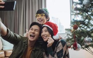 famiglia asiatica che prende selfie vicino all'albero di natale insieme a casa. famiglia, vacanze, concetto di natale foto