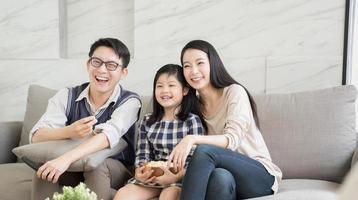 felice famiglia asiatica guardando la tv insieme sul divano in soggiorno. concetto di famiglia e casa foto