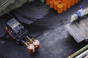 il carrello elevatore a forche dei barili di petrolio si sposta sul camion di trasporto che il lavoratore maschio organizza. foto