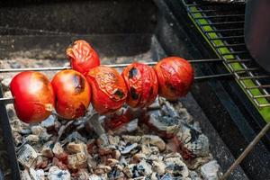 i pomodori freschi maturi vengono grigliati su uno spiedino su carboni ardenti. foto