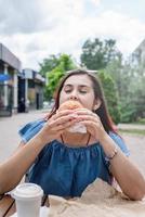 elegante donna millenaria che mangia hamburger al caffè di strada in estate foto