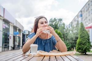 elegante donna millenaria che mangia hamburger al caffè di strada in estate foto