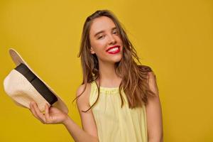 primo piano studio di adorabile donna adorabile con un sorriso perfetto in posa durante il servizio fotografico su sfondo giallo isolato e cappello di contenimento foto