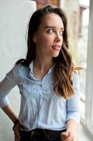 adorabile donna adorabile con lunghi capelli ondulati che indossa una camicia blu è seduta vicino alla finestra e distoglie lo sguardo con vista romantica. foto