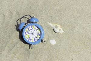 orologio blu e conchiglia sulla spiaggia foto