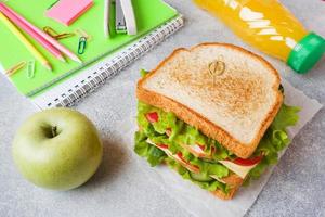 pranzo salutare per la scuola con panino, mela fresca e succo d'arancia. forniture scolastiche colorate assortite. copia spazio. foto