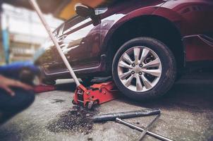 pneumatico dell'auto cambiato per la manutenzione in garage utilizzando il martinetto idraulico - concetto di manutenzione dell'auto foto