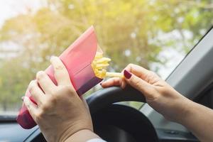 signora che mangia le patatine fritte bianche che guida l'auto pericolosamente foto