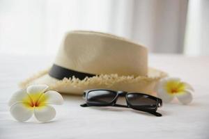 cappello di roba turistica occhiali da sole e fiore di plumeria in camera da letto bianca - felice vacanza relax vacanza e concetto di hotel foto