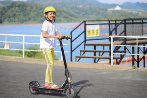 concetto di svago per i giovani. ritratto a figura intera di un ragazzo eccitato che cavalca un e-scooter nero al parco fluviale. foto