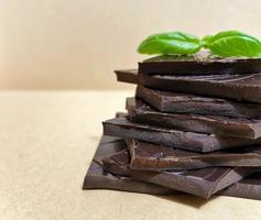 pezzi di primo piano di cioccolato fondente, inferiore e foglie di basilico verde foto