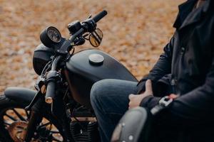 foto ritagliata di motociclista senza volto posa su una moto veloce, si ferma nel parco, terreno coperto di foglie cadute, si gode il viaggio e il viaggio. persone, stile di vita, concetto di trasporto.