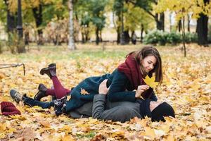 concetto di persone, tempo libero e stagione. la femmina e il maschio felici si divertono a passare del tempo insieme, sdraiati su un terreno coperto di foglie gialle. la ragazza e il ragazzo allegri si guardano felici l'un l'altro foto