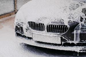 macchina nera che si lava con il sapone. concetto di lavaggio auto. automobile all'autolavaggio lavato con getto d'acqua a spruzzo. veicolo in schiuma. foto