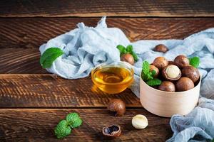 noci di macadamia in guscio con foglie di menta e miele su fondo di legno foto