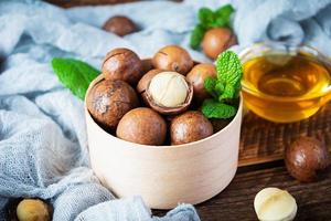 noci di macadamia in guscio con foglie di menta e miele su fondo di legno foto