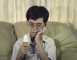 giovane asiatico con denti sensibili e gelato freddo perché mangia il gelato in soggiorno. foto