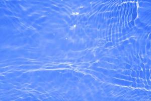 sfocatura sfocata trasparente di colore blu chiaro acqua calma superficie texture con schizzi e bolle. sfondo di natura astratta alla moda. onda d'acqua alla luce del sole con spazio di copia. struttura ad acquerello blu foto