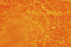 sfocatura sfocata acqua arancione che brilla nel mare. sfondo di dettagli d'acqua increspata. la superficie dell'acqua nel mare, sullo sfondo dell'oceano. onda d'acqua sotto il fondo di struttura del mare. foto
