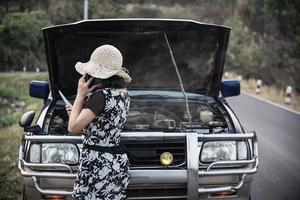 donna asiatica che chiama il riparatore o il personale assicurativo per risolvere un problema al motore di un'auto su una strada locale - persone con problemi di trasporto dell'auto concetto foto