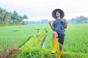 attraente giovane agricoltore asiatico allegro che si rallegra di avere successo nella coltivazione di risone nel campo di riso. concetto di agricoltura moderna. foto