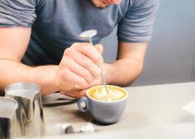 barista che usa la macchina per il caffè preparando caffè fresco o latte art e versandolo nella tazza bianca in caffetteria e ristorante, bar o pub foto