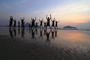 gruppo di giovani felici sagome che saltano sulla spiaggia sul bellissimo tramonto estivo foto