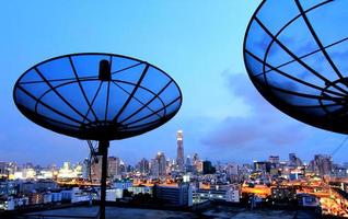 antenna parabolica nera di comunicazione sopra il cielo al tramonto nel paesaggio urbano foto