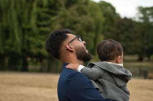 il padre pakistano asiatico tiene in braccio il suo bambino di 11 mesi nel parco locale foto