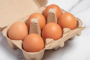 una scatola di cartone piena di uova di gallina fresche su sfondo bianco.