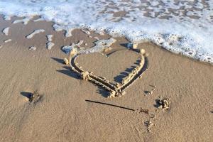 una bella forma di cuore dipinta nella sabbia di una spiaggia del Mar Baltico con alcune onde d'acqua. foto