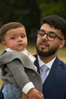 il padre pakistano asiatico tiene in braccio il suo bambino di 11 mesi nel parco locale foto