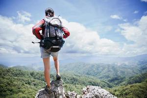 giovane donna escursionismo in piedi sulla roccia in alto, donna zaino che guarda la bellissima valle di montagna alla luce del sole in estate, paesaggio con ragazza sportiva, alte colline, foresta, cielo. viaggi e turismo. foto