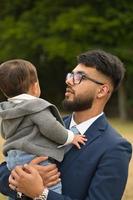 il padre pakistano asiatico tiene in braccio il suo bambino di 11 mesi nel parco locale foto