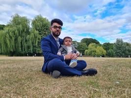 il padre pakistano asiatico tiene in braccio il suo bambino di 11 mesi nel parco locale foto