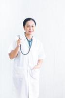 ritratto donna sicura e sorridente medico con uniforme bianca con il dispositivo medico stetoscopio su fondo nero bianco in ospedale. medico femminile asiatico nel settore sanitario dell'abito medico foto