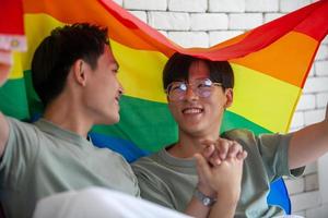 felice coppia gay asiatica che si tiene per mano insieme rilassandosi a casa sul letto, concetto lgbtq. foto