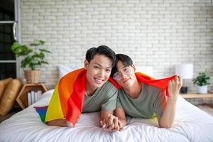 felice coppia gay asiatica che si tiene per mano insieme rilassandosi a casa sul letto, concetto lgbtq. foto