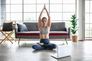 giovane donna asiatica che lavora e fa yoga con il computer portatile a casa, concetto sano. foto