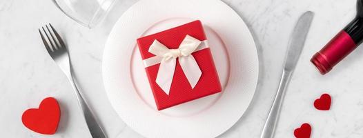 piatto con stoviglie, nastro, regalo e rose per il concetto di pasto speciale di San Valentino. foto