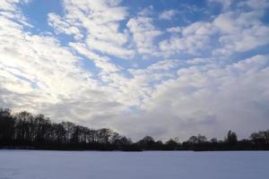 belle nuvole nel cielo che si affacciano su un campo agricolo innevato. foto