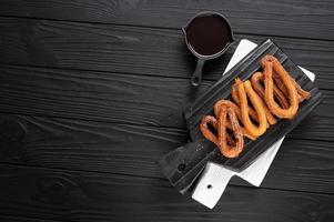 churros fatti in casa con cioccolato su fondo rustico di legno scuro. foto