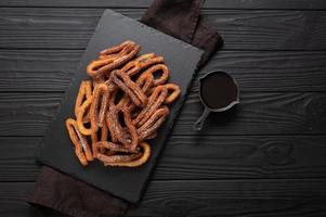 churros fatti in casa con cioccolato su fondo rustico di legno scuro. foto