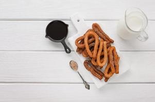 churros fatti in casa con cioccolato su fondo di legno bianco. foto