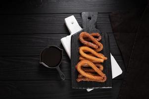 churros fatti in casa con cioccolato su fondo rustico di legno scuro. foto