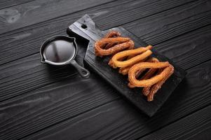 churros fatti in casa con cioccolato su fondo rustico di legno scuro. foto